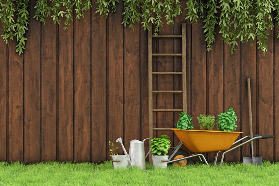 A garden fence with garden tools and a ladder against it.